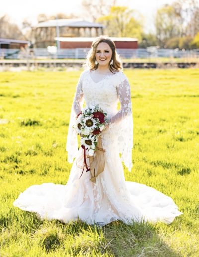 a woman in a wedding dress with a bouquet standing in a field