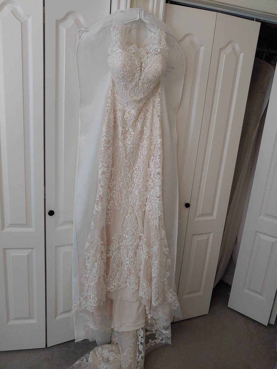 a wedding dress hanging up near a closet featuring a lace hem with netting border