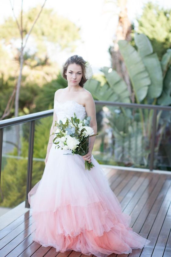 a woman standing on a balcony with a white and pink wedding dress holding flowers